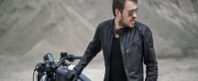 A man wearing motorcycle leather jacket and sitting on the harley bike