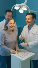 Dentist explaining dental instruments to a smiling female patient during a friendly consultation at a modern dental clinic