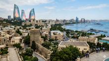 Wide panoramic view of Baku city featuring the historic Old City walls, Flame Towers, modern skyline, and Caspian Sea coastline under a clear sky.