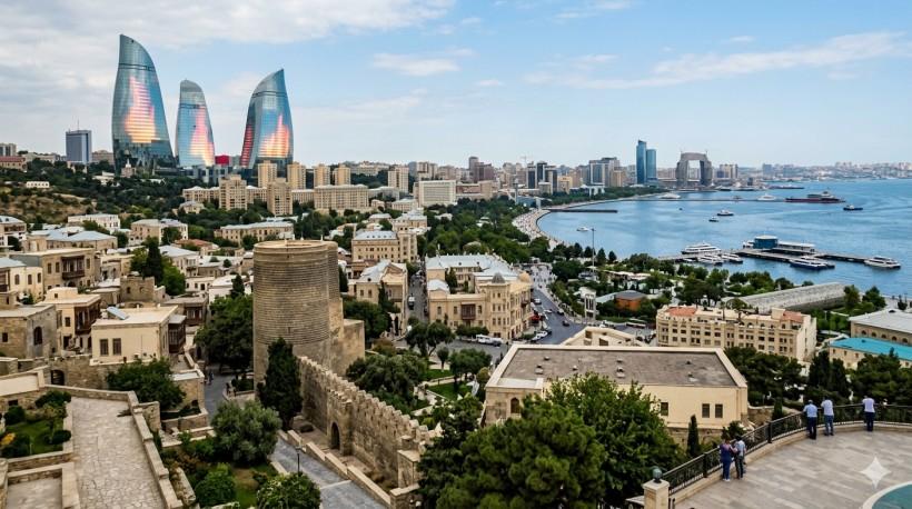Wide panoramic view of Baku city featuring the historic Old City walls, Flame Towers, modern skyline, and Caspian Sea coastline under a clear sky.